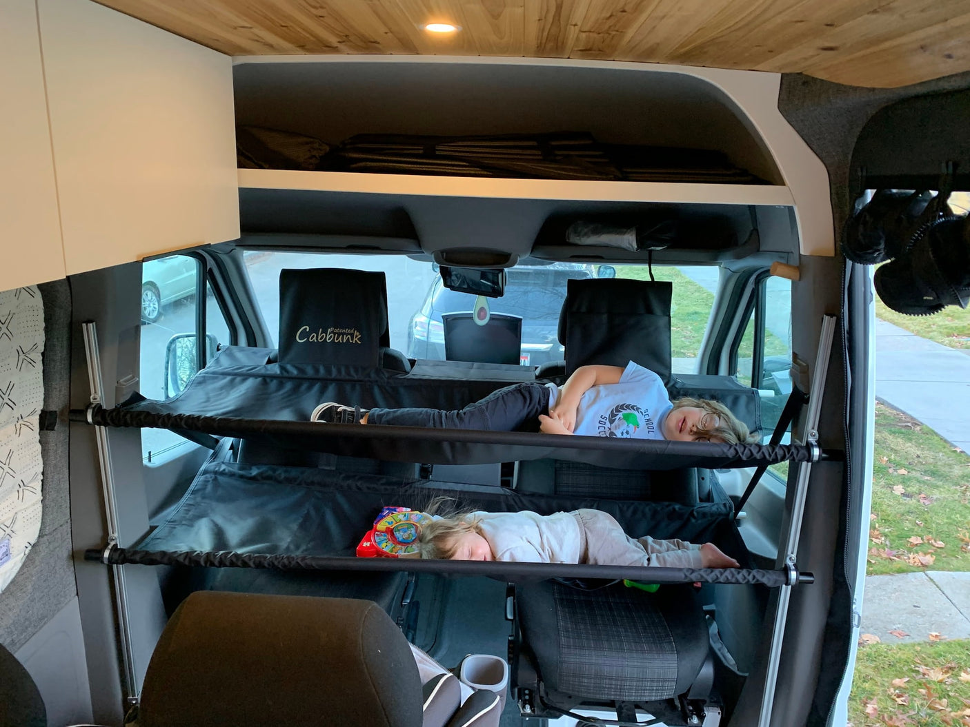 Two children sleep comfortably in suspended cab bunk beds in an rv rental van. Clever solution for family travel!