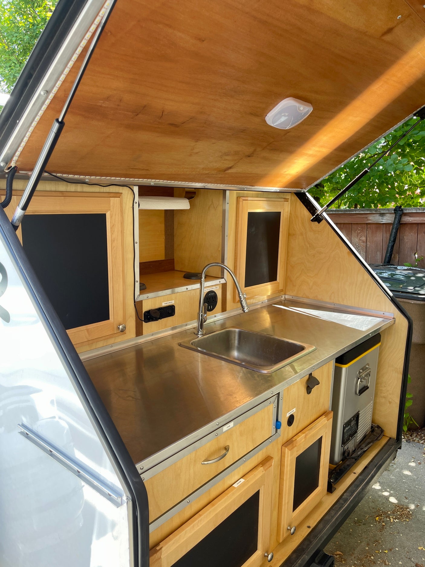 Compact RV rental kitchen with stainless sink, fridge, wood cabinets, and LED lighting.