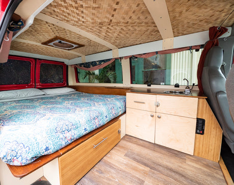 Inside an RV rental: a modern camper van conversion featuring a comfy bed, compact kitchen, and woven ceiling.