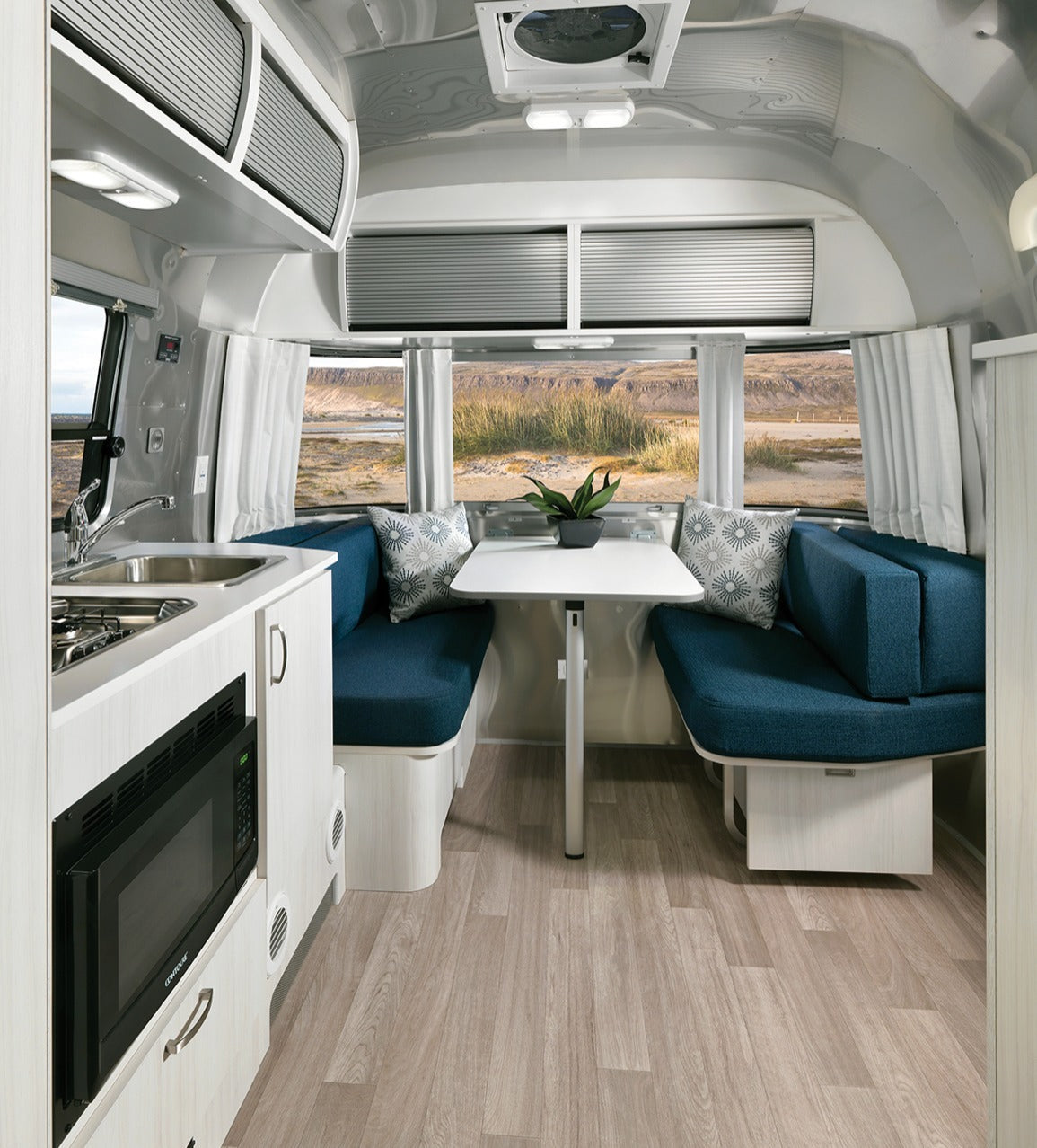 Modern RV rental interior with a fully equipped kitchenette, comfortable dining booth, and large windows showcasing outdoor views.