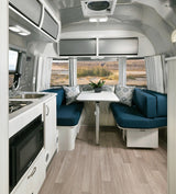 Modern RV rental interior with a fully equipped kitchenette, comfortable dining booth, and large windows showcasing outdoor views.