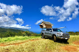 An RV rental alternative: silver pickup truck with rooftop tent and awning on a scenic mountain-ocean view.