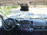 RV rental cockpit view: dashboard, steering wheel, and front windshield looking out to a wooded road.