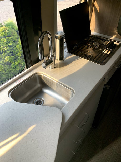 This RV rental kitchen features a sleek stainless steel sink, gas stove, and convenient pop-up power outlet on light counters.