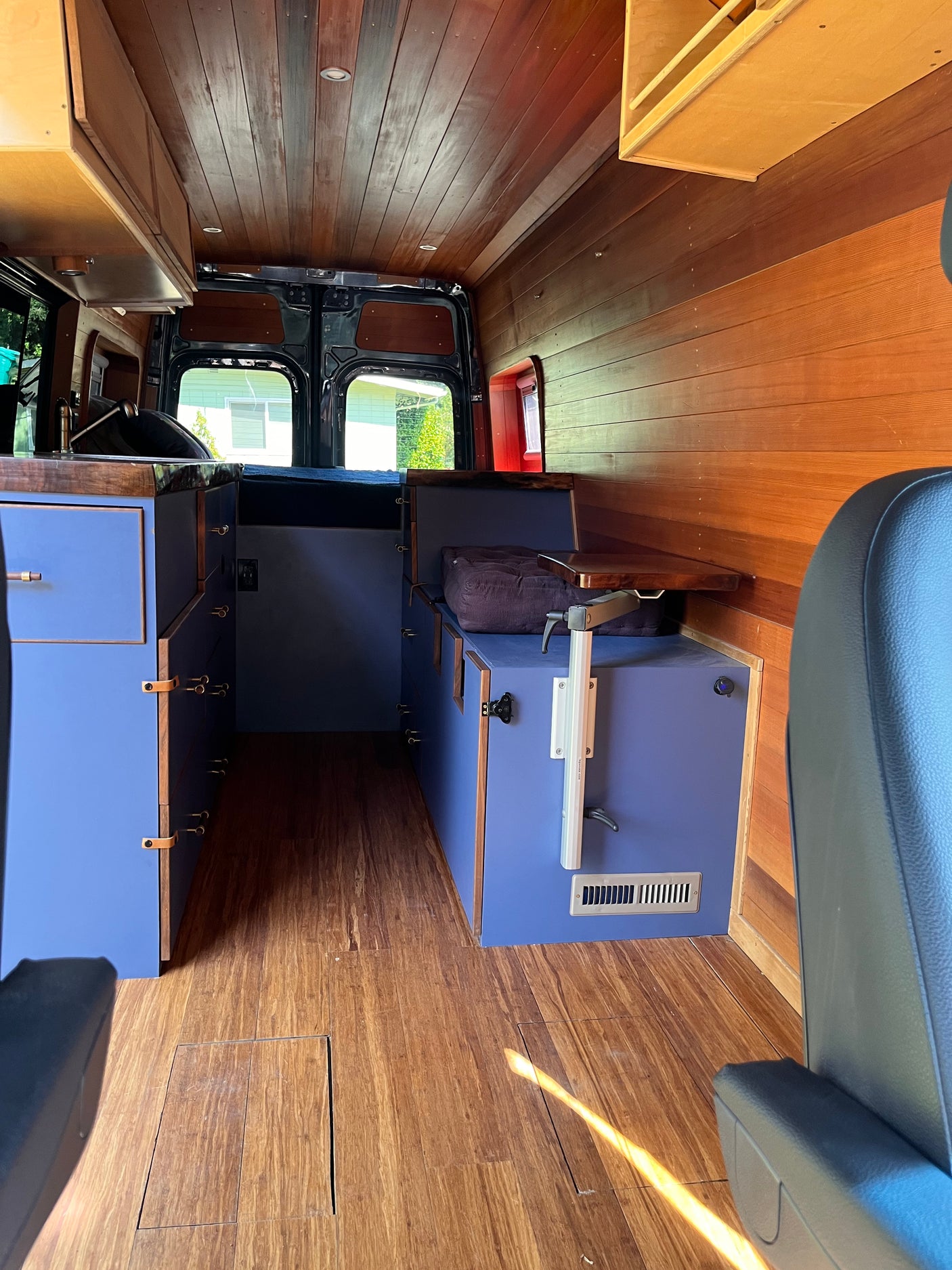 Customized RV rental interior showcasing wood paneling, floor, blue cabinets, and seating for comfortable travel.