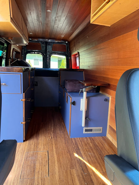 Customized RV rental interior showcasing wood paneling, floor, blue cabinets, and seating for comfortable travel.