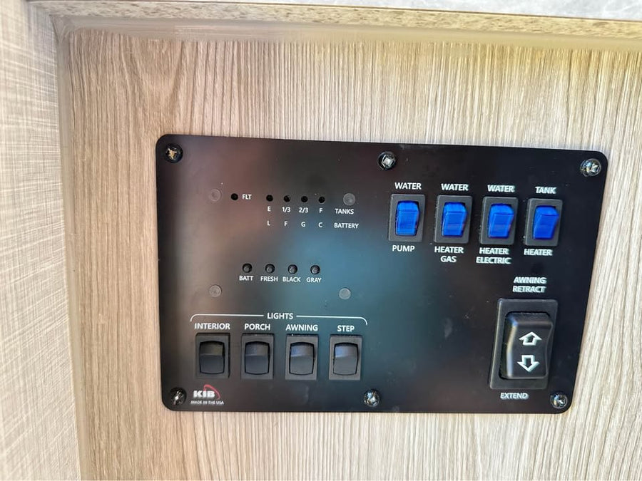 RV rental control panel: Black panel on wood, featuring switches for water pump, heaters, lights, awning, and tank/battery levels.