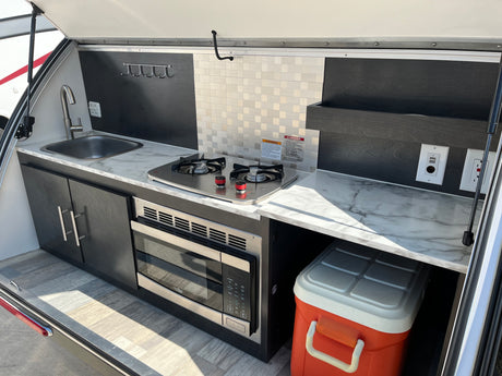 This RV rental features a compact outdoor kitchen with a sink, stove, microwave, and cooler, perfect for camping.