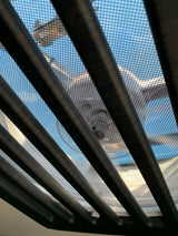 View from an RV rental looking up through dark blinds and a screen at a colorful kite and blue sky.