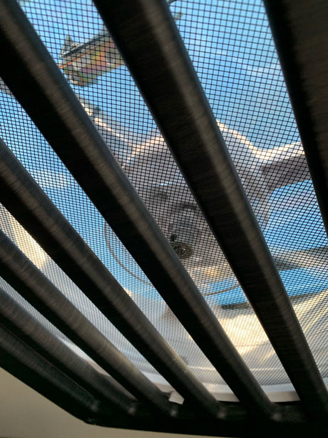 View from an RV rental looking up through dark blinds and a screen at a colorful kite and blue sky.