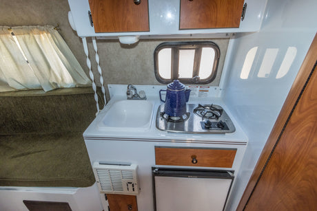 Explore this RV rental's compact interior featuring a kitchenette with sink, stove, mini-fridge, and cozy sleeping bench.