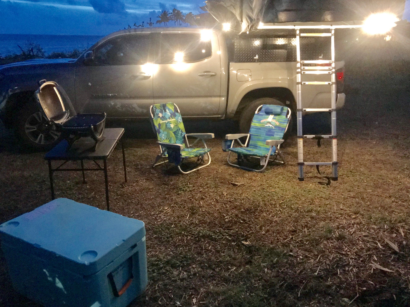 Coastal RV rental alternative: a truck with rooftop tent, chairs, cooler, and grill set for evening camping.