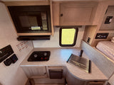 Inside a Palomino RV rental: a compact kitchen with microwave, two-burner stove, sink, and controls.
