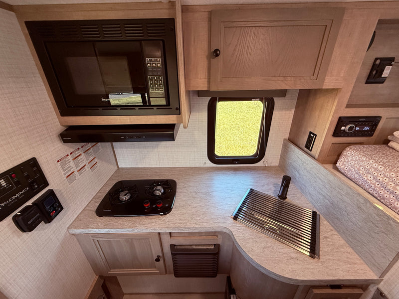 Inside a Palomino RV rental: a compact kitchen with microwave, two-burner stove, sink, and controls. — photo 5