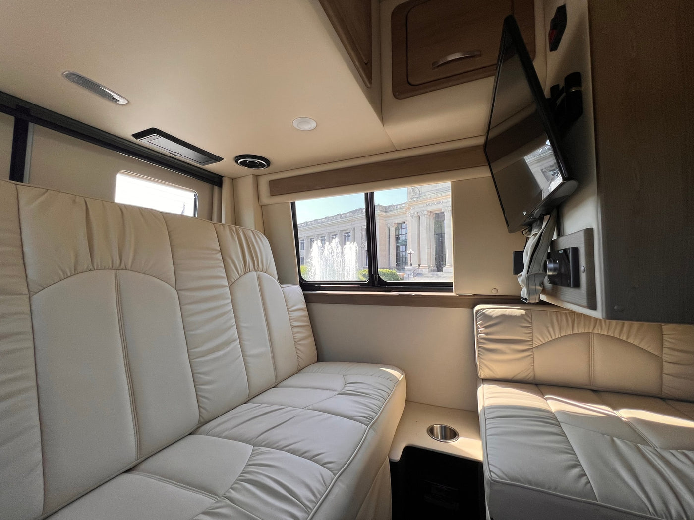 Comfortable RV rental interior: ample light seating, TV, and a bright window showcasing a grand building and a beautiful fountain. — photo 7