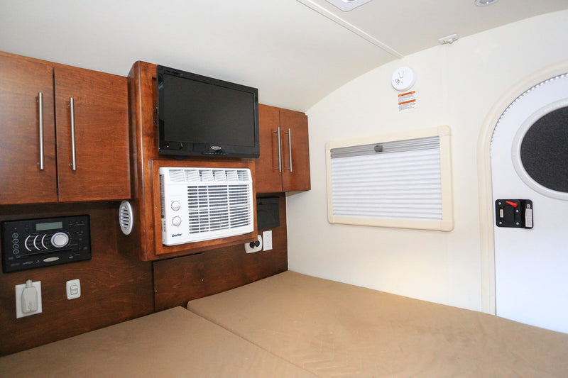 Inside an RV rental, a cozy bed, wood cabinets, TV, AC unit, and control panel provide comfortable amenities. — photo 4