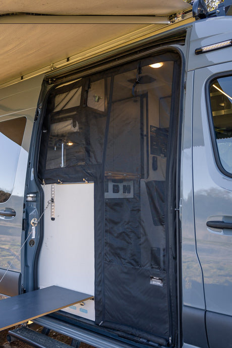 Open side door of an RV rental showing bug screen, interior sink, pull-out table, and extended awning for comfort.