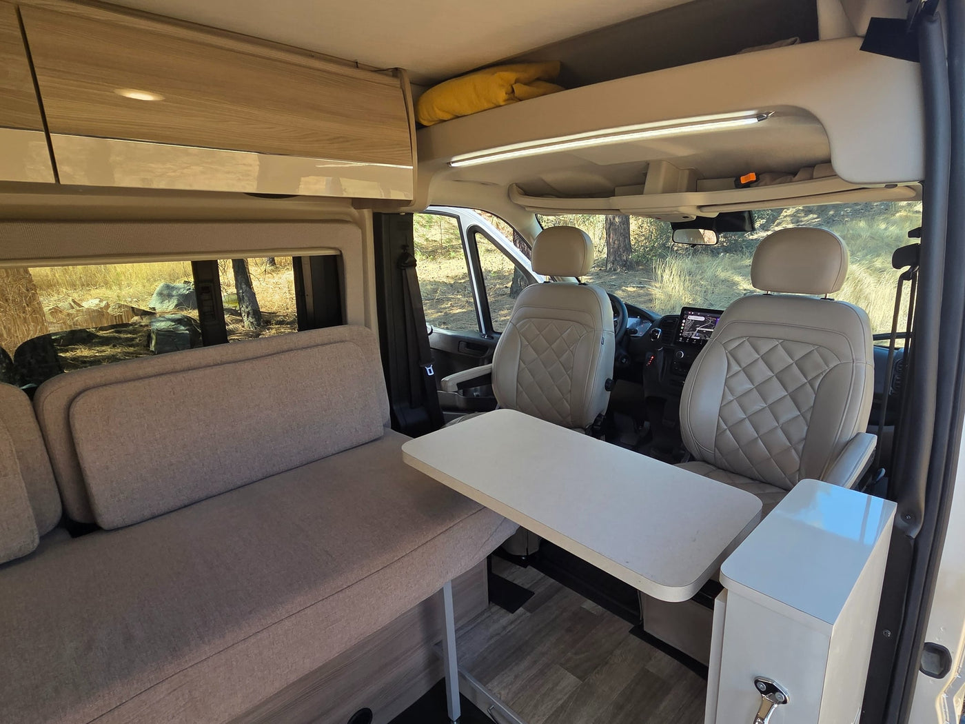  evoking a classic road trip.|Silver rv rental camper van and camping setup in a vast desert landscape with sandstone formations under cloudy skies.|An RV rental brings comfort to desert camping. A person and dogs relax by a van amid impressive rock formations.|An rv rental camper van with open door and a woman relaxing outside at night under the moon. Ideal for outdoor adventures.|Inside this modern RV rental: comfortable sofa — photo 6
