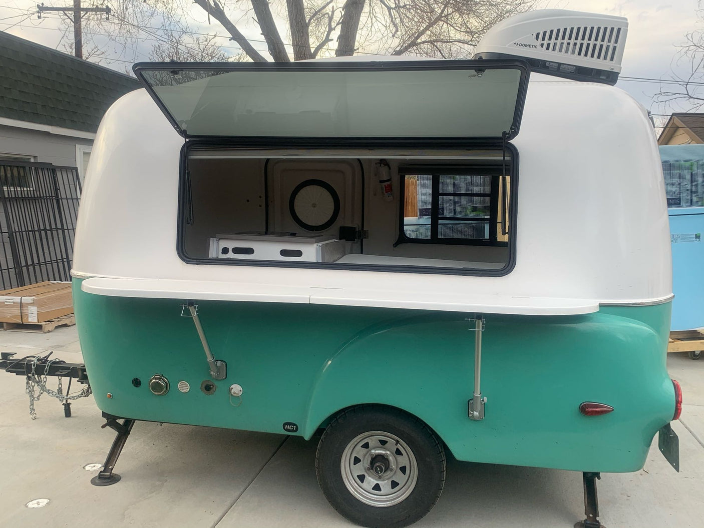 This compact teal & white camper trailer, featuring an open serving hatch & AC unit, is ideal for an RV rental.