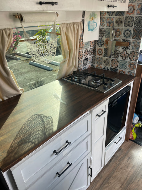 Rv rental kitchen: gas stove, patterned tiles, white cabinets, and bright window view of outdoor parking.
