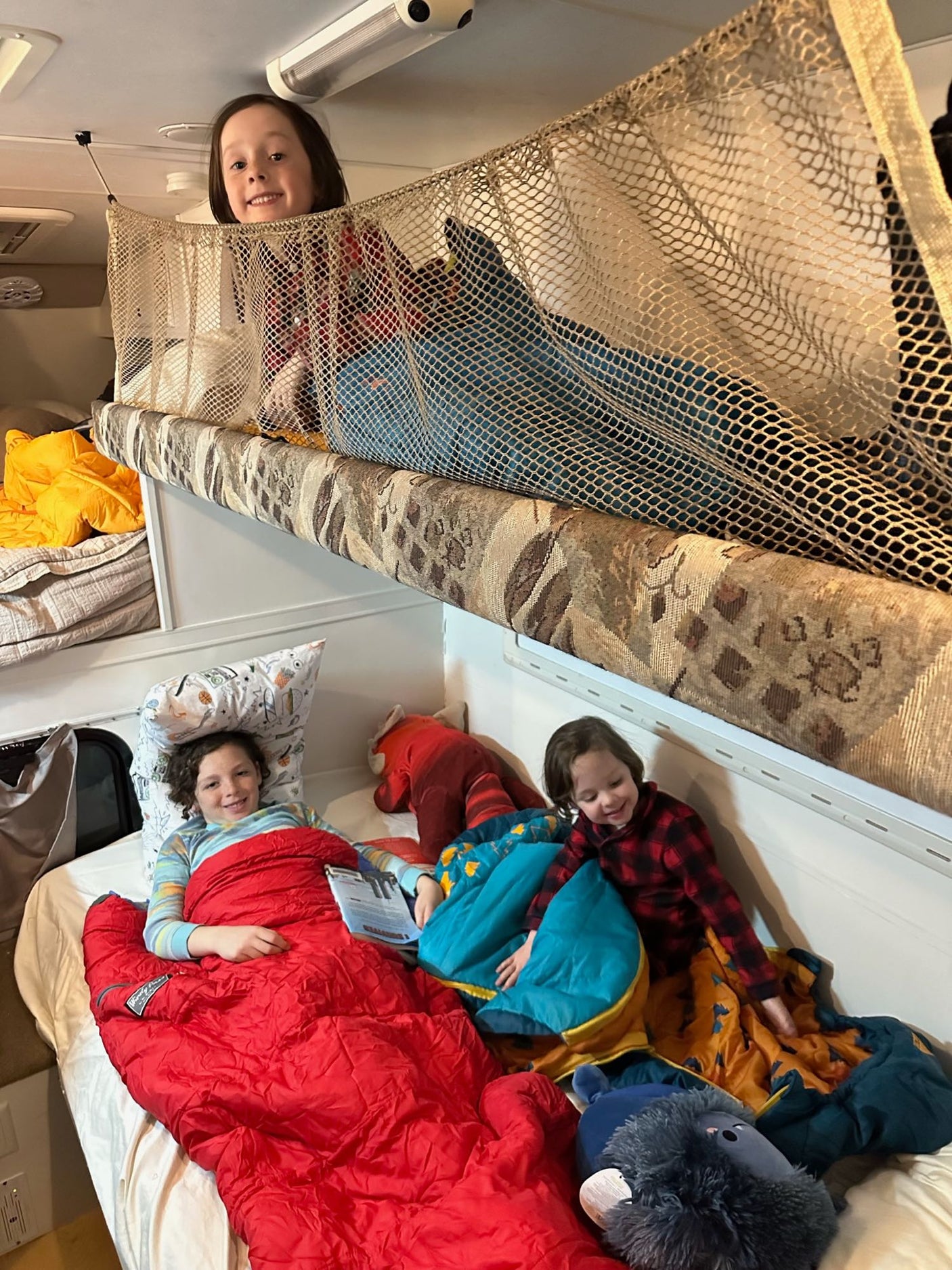 Happy kids in their RV rental bunks, enjoying cozy sleeping bags during a family road trip.