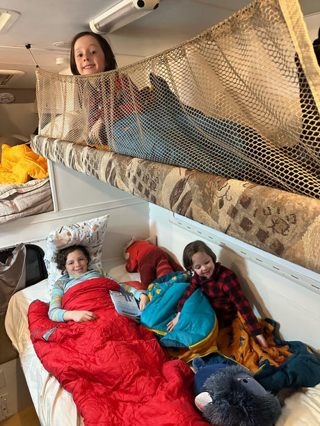Happy kids in their RV rental bunks, enjoying cozy sleeping bags during a family road trip.
