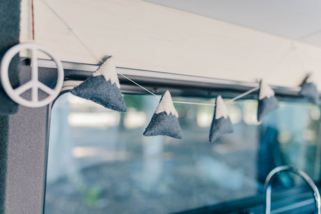 Inside an RV rental: a white peace sign & felt mountain garland adorn the window, adding a touch of travel charm.
