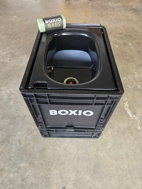 This black BOXIO portable toilet, with a roll of "BOXIO BAGS" on top, is ready for your RV rental adventures.