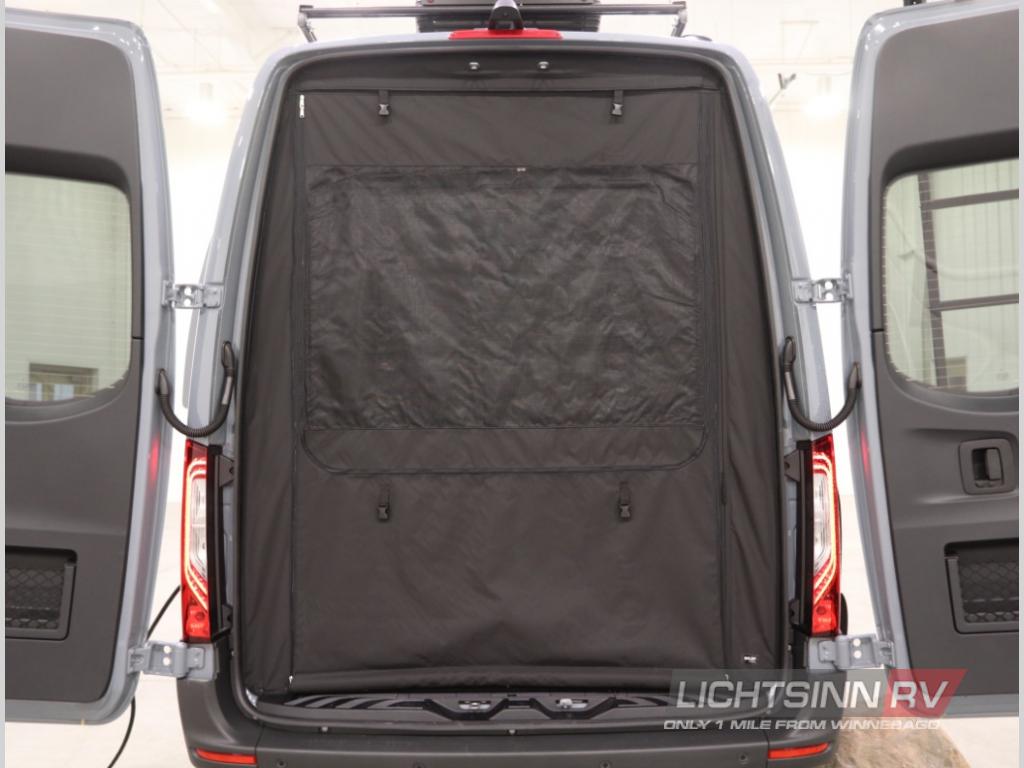 Rear view of an RV rental van with open back doors and a black fabric interior screen, showing cargo space.