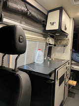This RV rental features a compact kitchen with a sink, counter, and fridge. Overhead storage & window blinds visible. Ideal for travel.