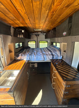Cozy rv rental interior featuring a wooden ceiling, comfy bed, kitchen sink, and storage cabinets for an enjoyable road trip.