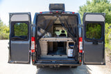 Open back doors of an RV rental reveal a custom interior with a bed, storage, and mosquito screen for outdoor adventures.