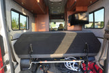 Bright RV rental interior with a convertible rear bed, under-seat storage, side windows, and a mounted TV.