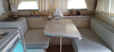 A vintage RV rental interior: a dining booth with light cushions, center table, and eclectic decor on the shelf.