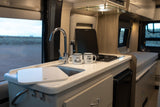 Compact RV rental kitchen with a sink, stovetop, and two camping mugs, ready for adventure.