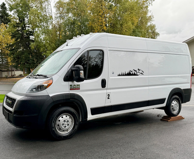 White Ram ProMaster camper van for rv rental, featuring a mountain decal and parked on leveling blocks. — photo 2