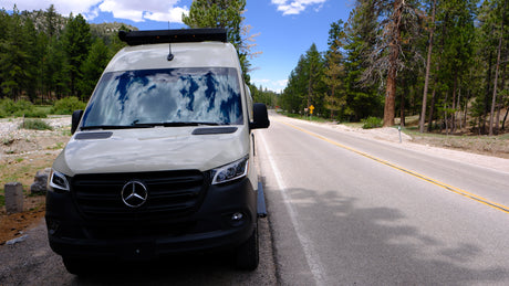 This Mercedes Sprinter RV rental is perfect for a scenic road trip through mountain forests. Clouds reflect on its windshield.
