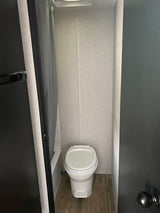 An RV rental's compact bathroom, featuring a white toilet, light walls, and wood-look floor.