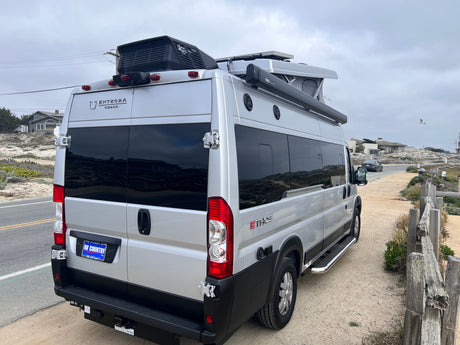 An Entegra Ethos camper van, an excellent rv rental option, parked on a dirt path along a coastal road.