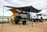 This XTR teardrop **rv rental** and Jeep Gladiator create a perfect lakeside overlanding camp, with an awning, table, and chair.