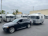 Black Audi SUV towing a shining Airstream RV rental, one of many travel trailers on a cloudy day.