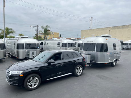 Black Audi SUV towing a shining Airstream RV rental, one of many travel trailers on a cloudy day.