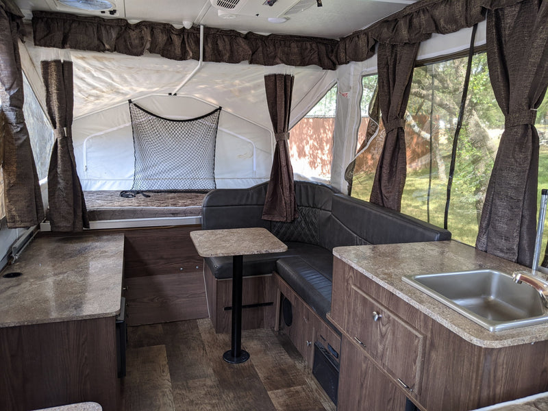 Spacious pop-up RV rental interior featuring a dinette, kitchen with sink, and sleeping area with privacy curtains. — photo 6