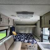 This RV rental interior offers a bed with camo bedding, a comfy sofa, and a small kitchen area, ideal for journeys.