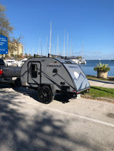 Grey Freesolo teardrop rv rental hitched to a truck, parked by a marina filled with sailboats. Ideal for outdoor adventures.
