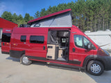 Vibrant red Winnebago Solis campervan, ideal for rv rental travel. Pop-top raised, interior visible through open door.