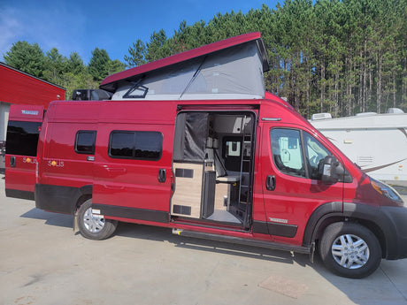 Vibrant red Winnebago Solis campervan, ideal for rv rental travel. Pop-top raised, interior visible through open door.