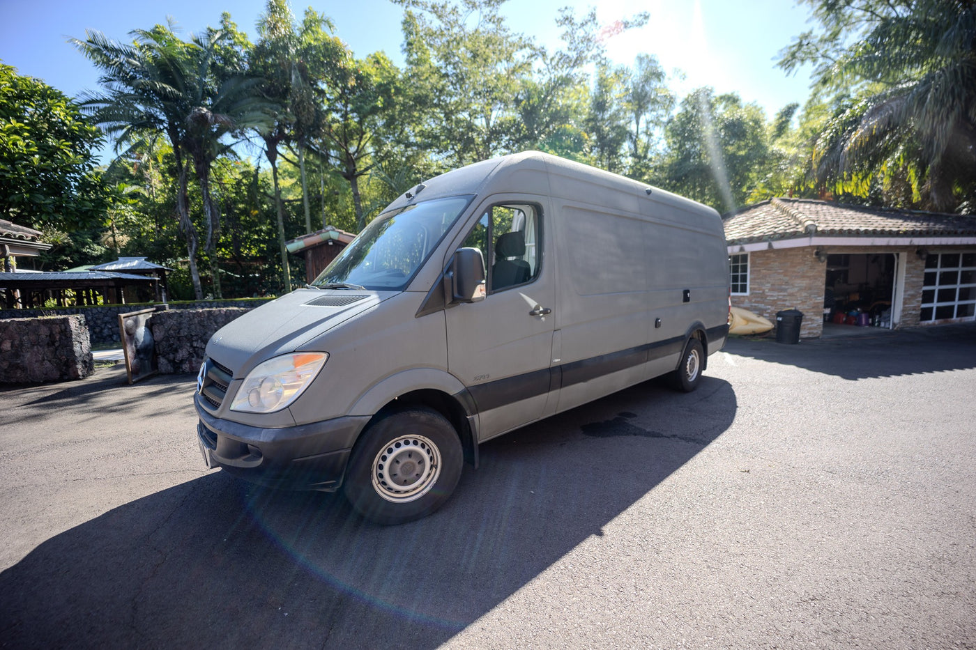 This grey Mercedes Sprinter camper van, ideal for rv rental, is parked on an asphalt driveway amidst tropical greenery and buildings. — photo 11