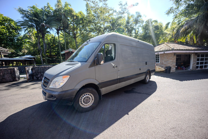 This grey Mercedes Sprinter camper van, ideal for rv rental, is parked on an asphalt driveway amidst tropical greenery and buildings. — photo 11