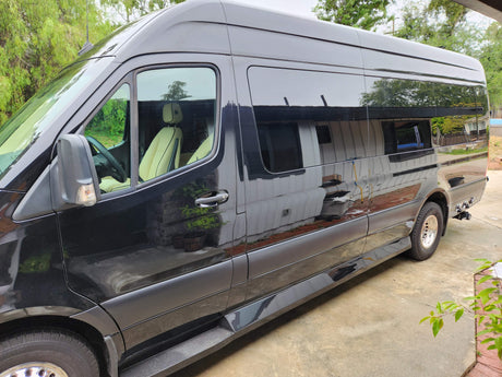 Side view of a glossy black luxury Sprinter van, ideal for rv rental. Parked on concrete with tinted windows and cream seats.